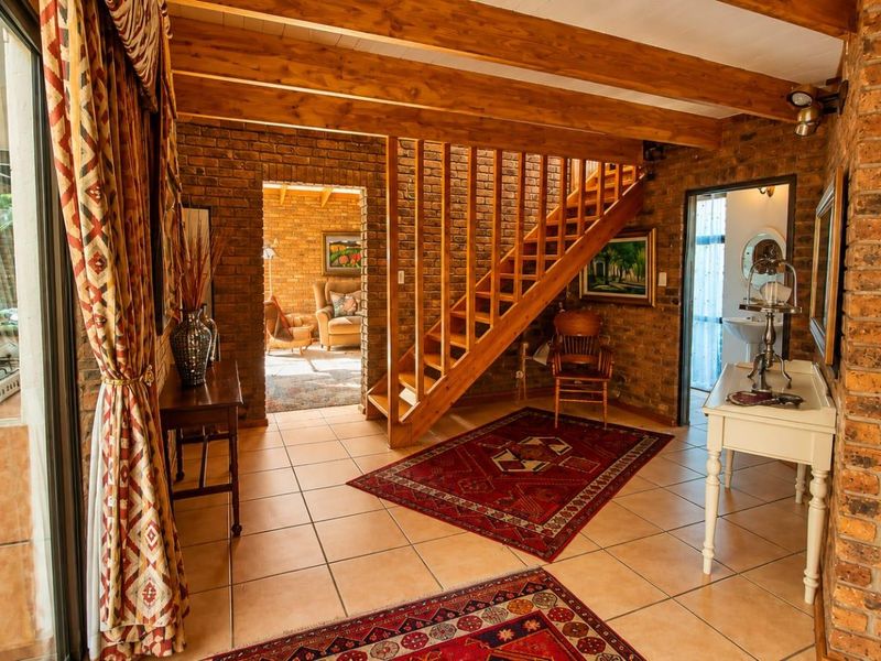 Spacious living area featuring rustic face brick walls, exposed timber ceiling beams, tiled flooring, and a wooden staircase leading to the upper level.