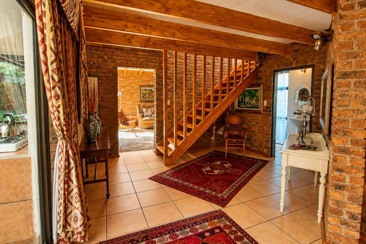 Spacious living area featuring rustic face brick walls, exposed timber ceiling beams, tiled flooring, and a wooden staircase leading to the upper level.