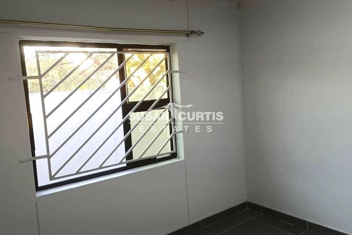 A simple bedroom featuring tiled flooring, a window with security bars, and a curtain rod.