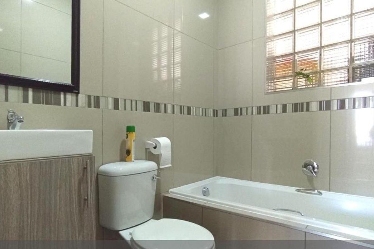 A modern bathroom featuring neutral wall tiles, a built-in bathtub, a vanity with a basin, and a glass block window for natural light.