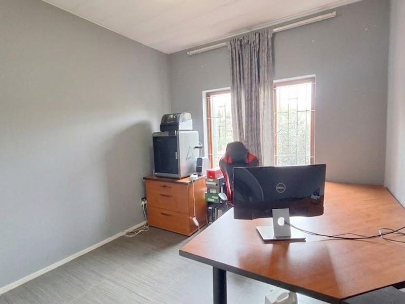 A functional bedroom or home office space featuring tiled flooring and windows fitted with security bars.