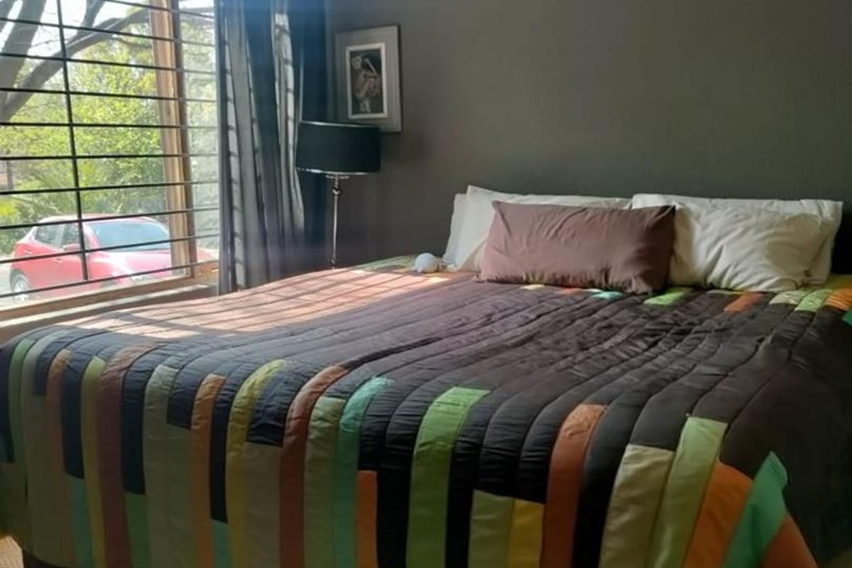 A bedroom featuring dark painted walls, carpeted flooring, and a large window fitted with security bars.
