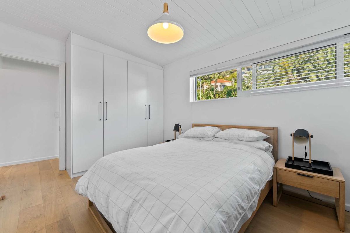 A bright and modern bedroom featuring timber flooring, a white tongue and groove ceiling, and ample built-in wardrobe storage.