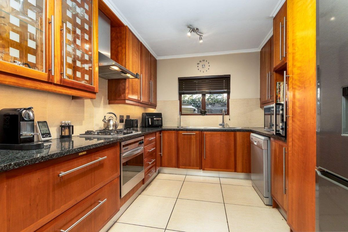 A well-maintained kitchen featuring warm wooden cabinetry, granite countertops, a gas hob, built-in oven, and tiled flooring with a functional layout.