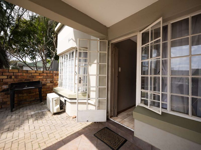 A paved outdoor patio area featuring a brick boundary wall, air conditioning unit, and direct access to the interior through steel-framed doors.