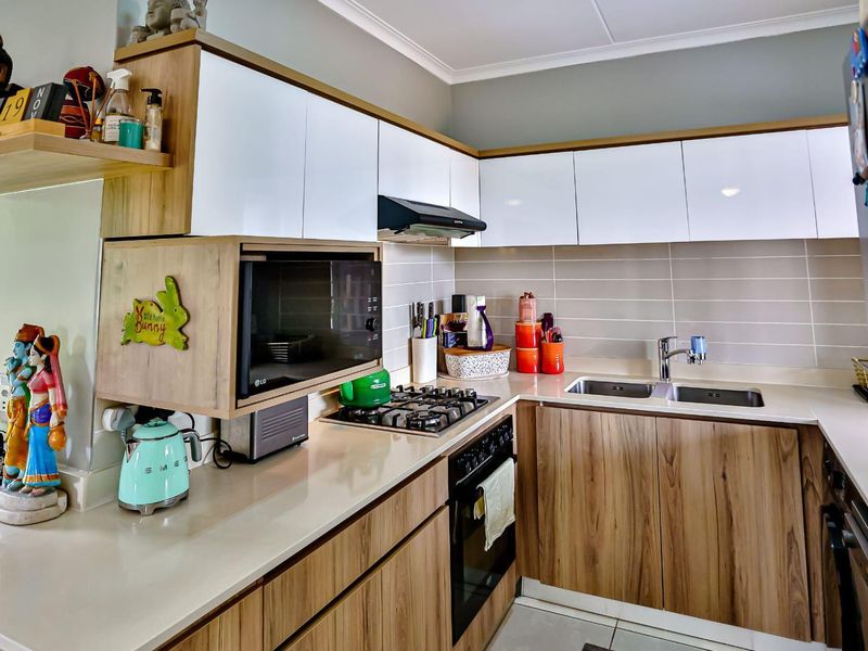 Modern kitchen featuring wood-grain and white cabinetry, stone countertops, gas hob, built-in oven, and a double bowl sink with a tiled backsplash.