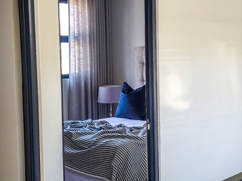 A view into a bedroom featuring neutral wall tones, tiled flooring, and window treatments, captured through a doorway.