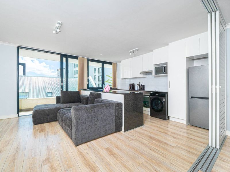 Modern open-plan living area featuring a sleek kitchen with granite island, built-in appliances, and large sliding doors leading to a balcony.