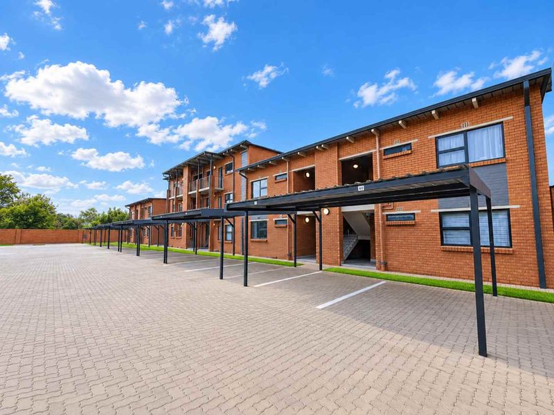 A well-maintained apartment complex exterior featuring a paved parking area with covered carports and a modern brick facade.