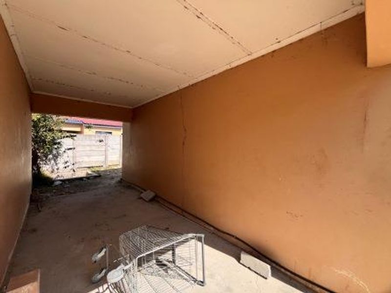 A covered outdoor patio area featuring concrete flooring and ceiling, showing visible wall cracking and signs of wear.