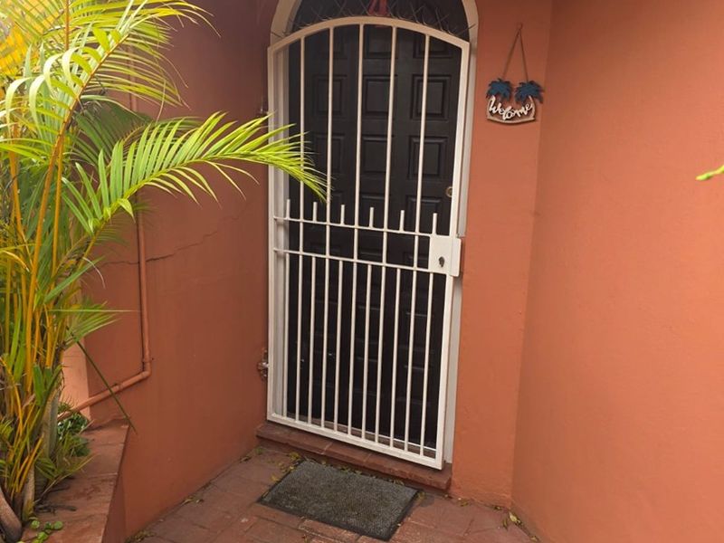 A private entrance area featuring a secure arched door with a white metal security gate and brick paved flooring.