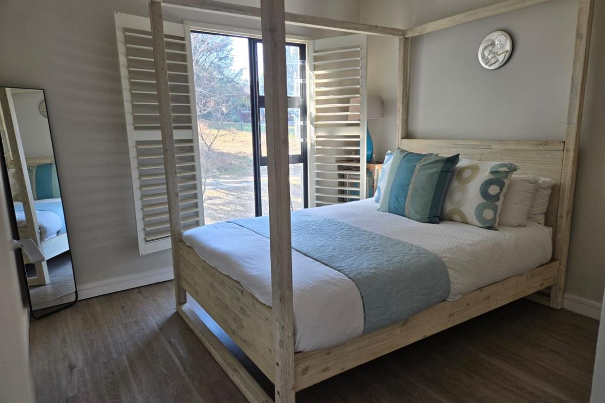 A well-maintained bedroom featuring light wood-look flooring and white plantation shutters on the window, providing a bright and airy atmosphere.