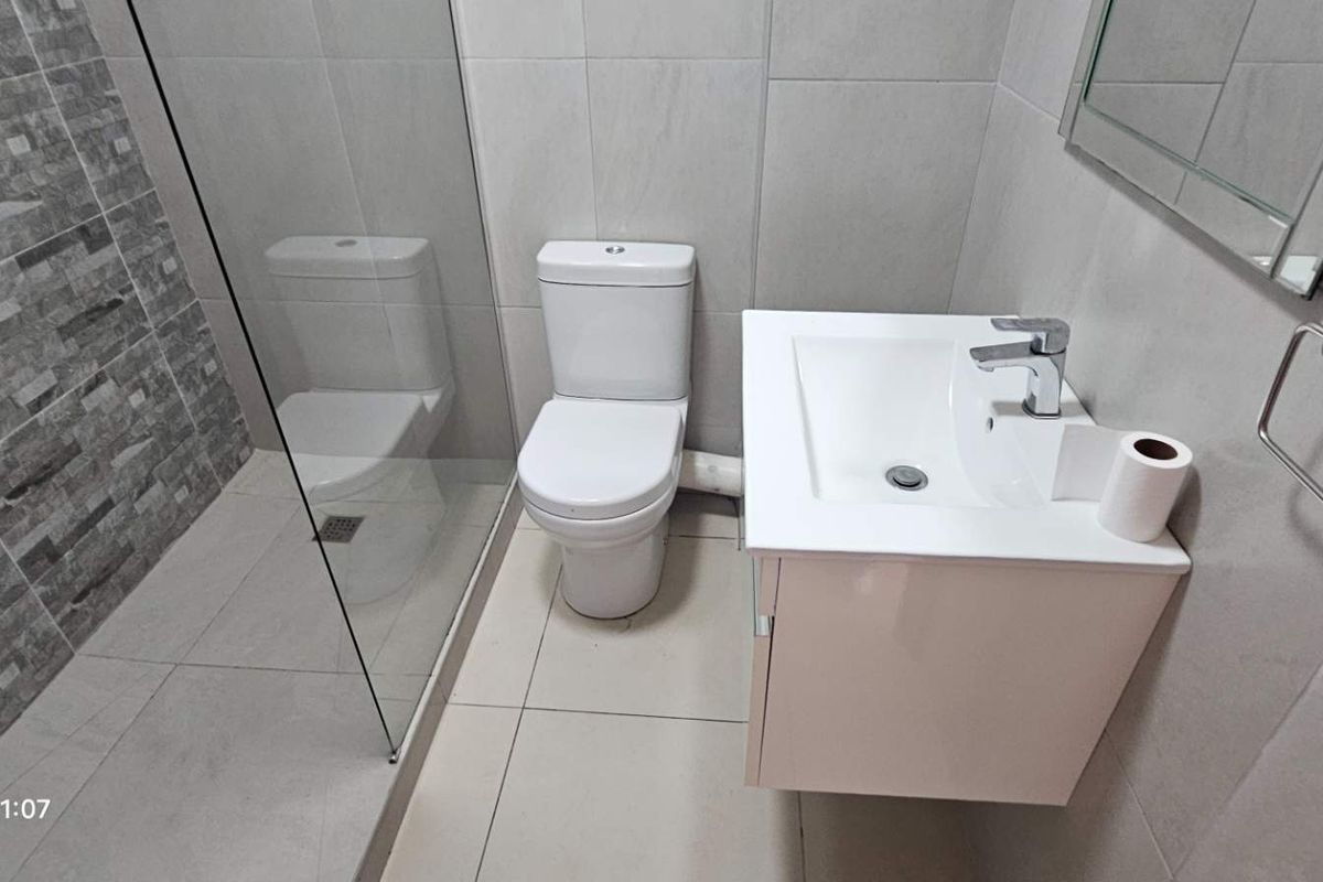 A modern, compact bathroom featuring a glass-enclosed shower, wall-mounted vanity with basin, and neutral tiled finishes throughout.