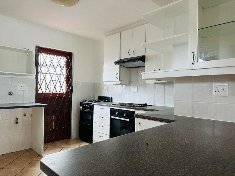 A functional kitchen featuring built-in cabinetry, laminate countertops, a gas hob, and an integrated oven, with direct access to an exterior security door.