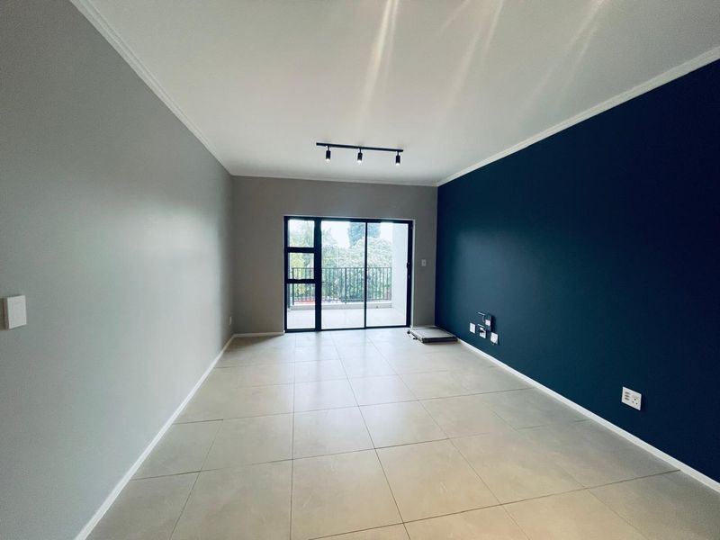 A bright, empty living room featuring large format floor tiles, a striking dark blue accent wall, and sliding glass doors leading to a balcony.