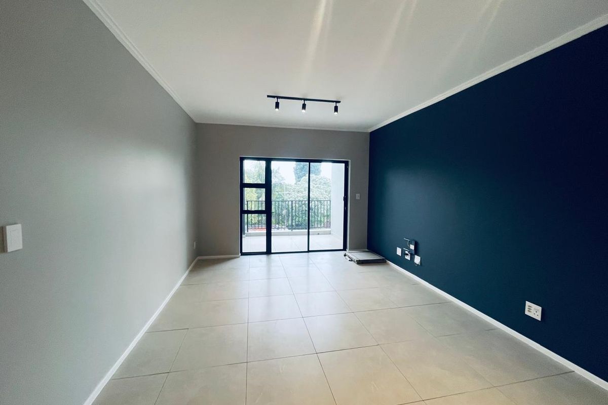 A bright, empty living room featuring large format floor tiles, a striking dark blue accent wall, and sliding glass doors leading to a balcony.