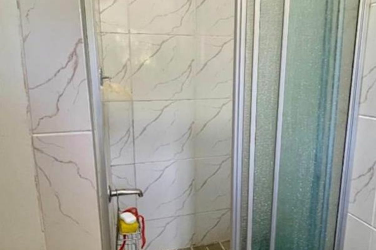 A functional shower enclosure featuring marble-effect wall tiles, a raised tiled base, and a sliding glass door.