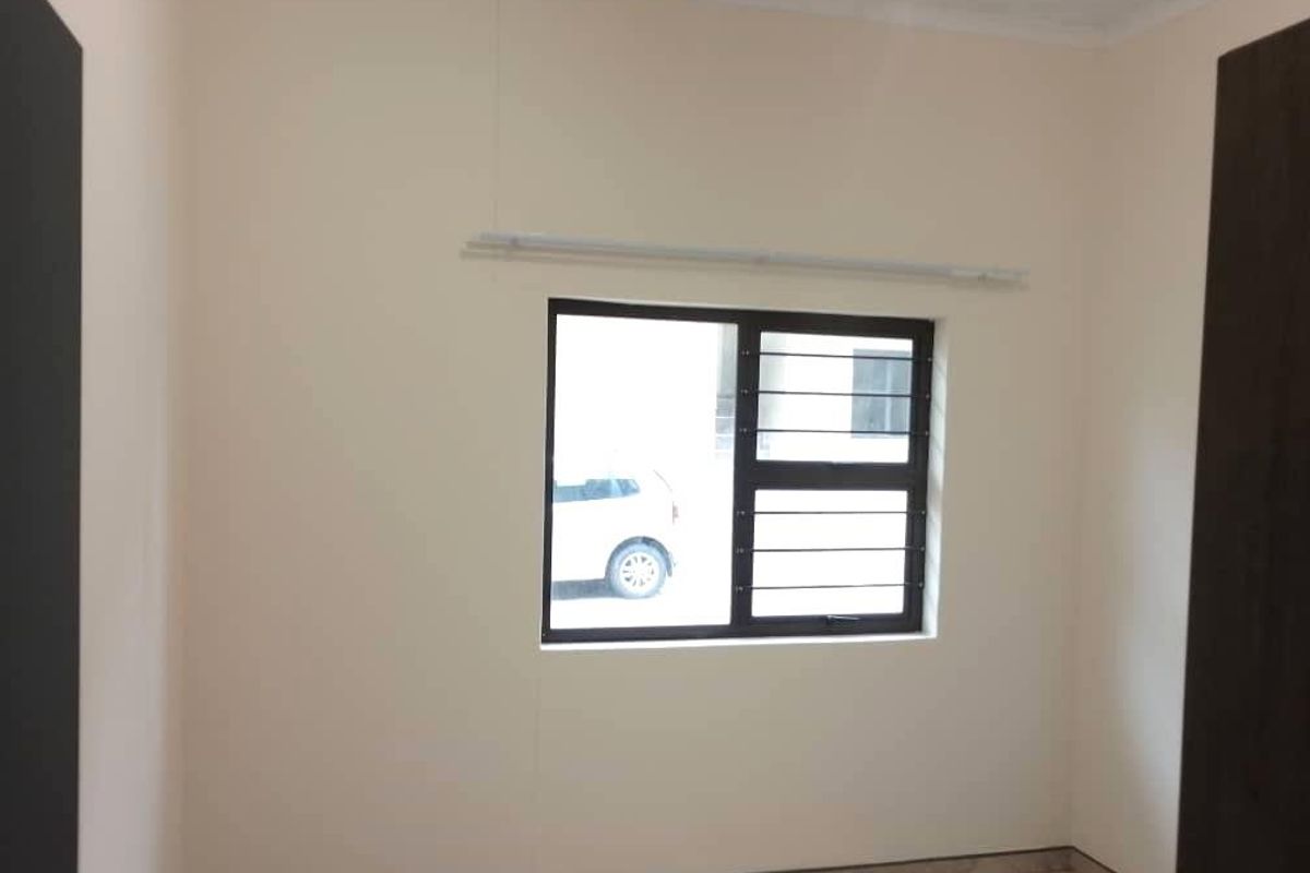 A clean, empty bedroom featuring neutral walls, tiled flooring, and a window fitted with security bars.