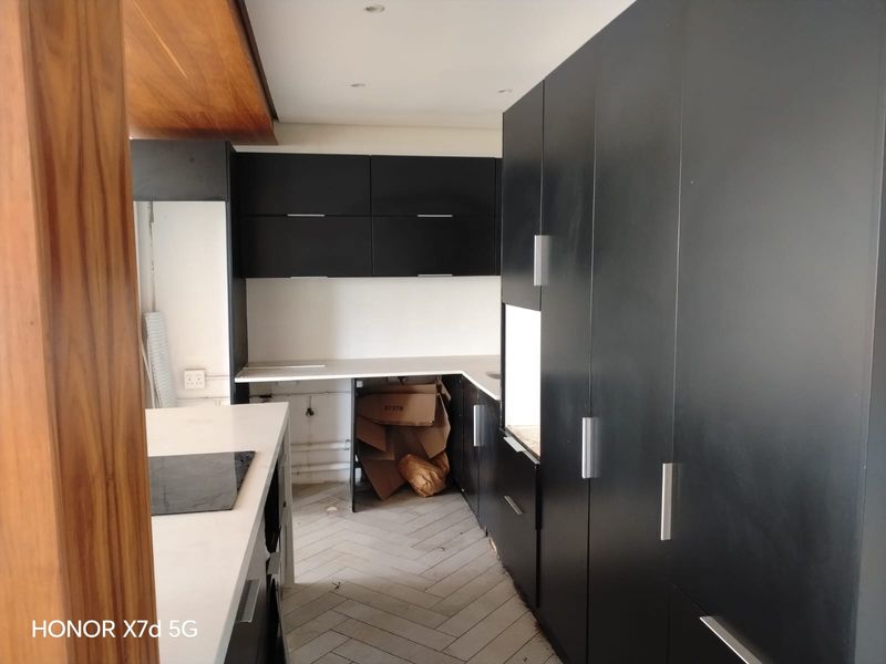 A modern kitchen featuring matte black cabinetry, stone countertops, and herringbone flooring, currently in an unfinished state requiring completion of fixtures and cabinetry.