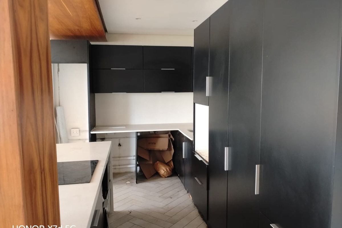 A modern kitchen featuring matte black cabinetry, stone countertops, and herringbone flooring, currently in an unfinished state requiring completion of fixtures and cabinetry.