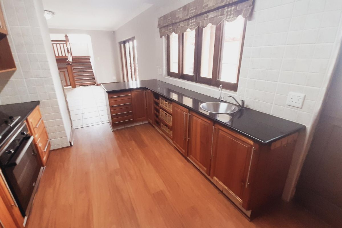 A functional kitchen featuring wooden cabinetry, dark countertops, a built-in oven, and a stainless steel sink, with tiled backsplash and wood-look flooring.