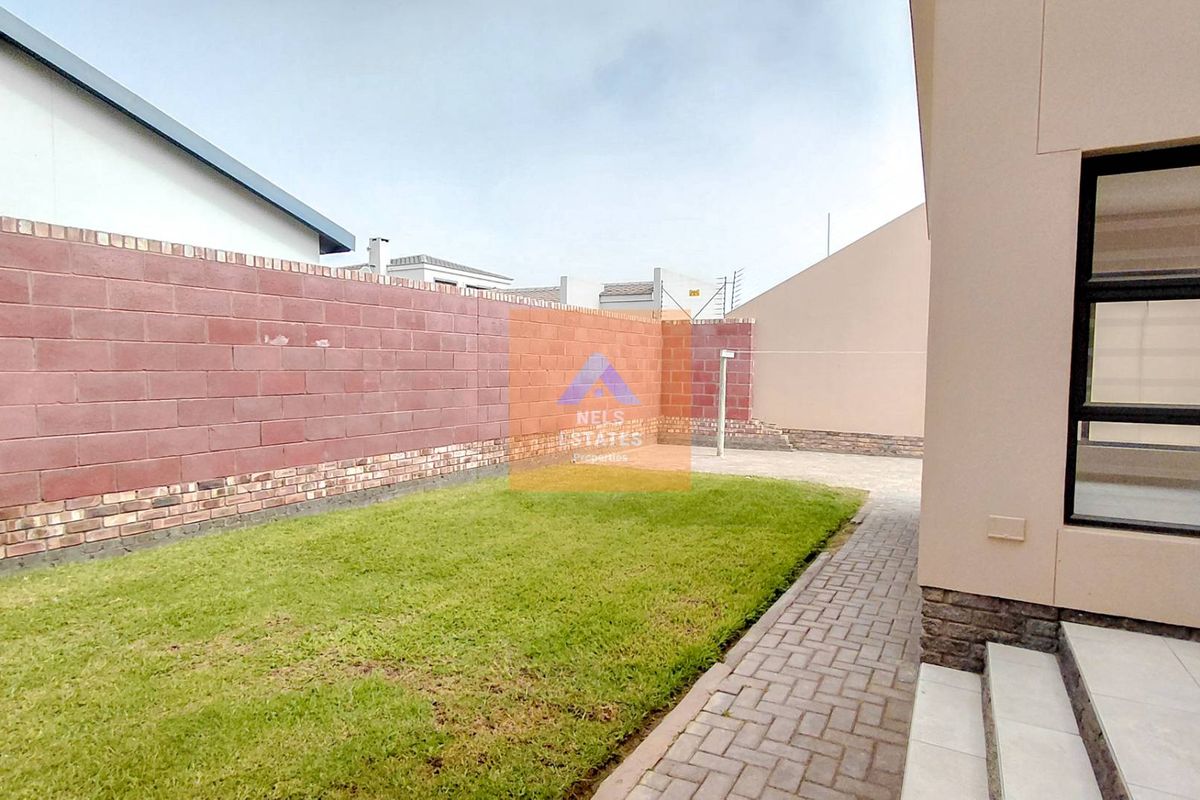 A private rear garden featuring a manicured lawn, paved walkway, and high brick boundary walls, accessible via a sliding door.