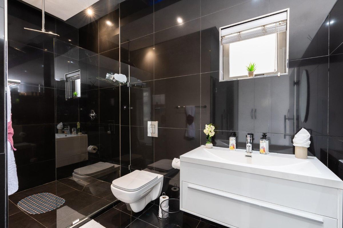 Modern bathroom featuring high-gloss black wall tiles, a floating vanity with integrated basin, and a spacious glass-enclosed shower with a rain shower head.