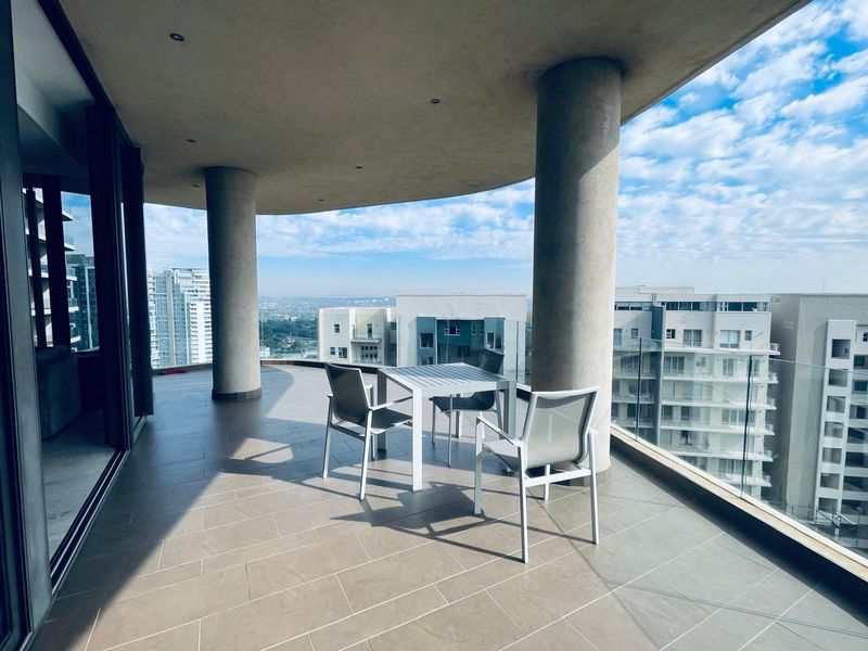 Spacious covered balcony featuring modern tiled flooring, a sleek glass balustrade, and expansive city views, perfect for outdoor relaxation.
