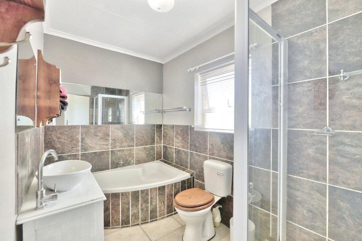 A functional bathroom featuring a built-in bathtub, separate glass-enclosed shower, vanity with basin, and tiled wall finishes.
