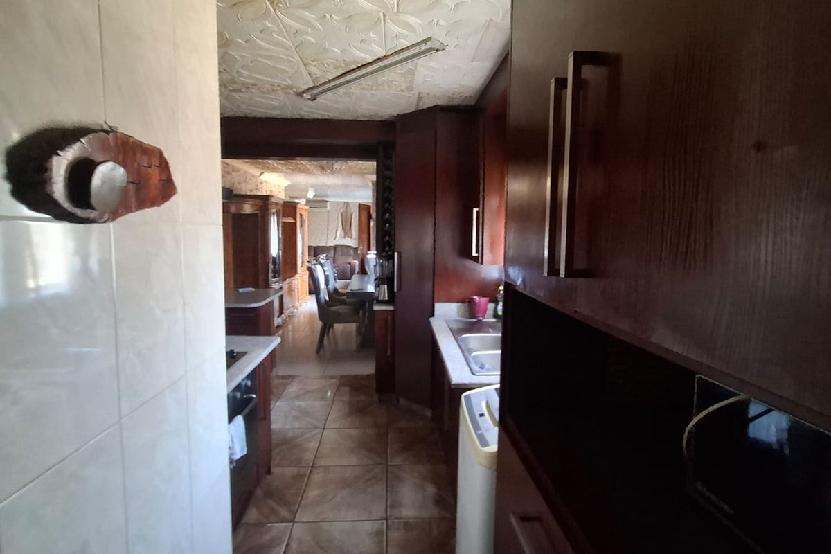 A dated kitchen featuring dark wood cabinetry, tiled flooring, and a textured ceiling, with a view leading into the adjacent dining area.