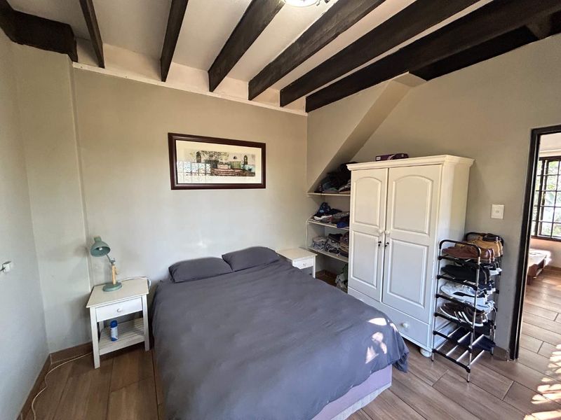 A cozy bedroom featuring exposed timber ceiling beams and tiled flooring, offering a rustic cottage aesthetic.