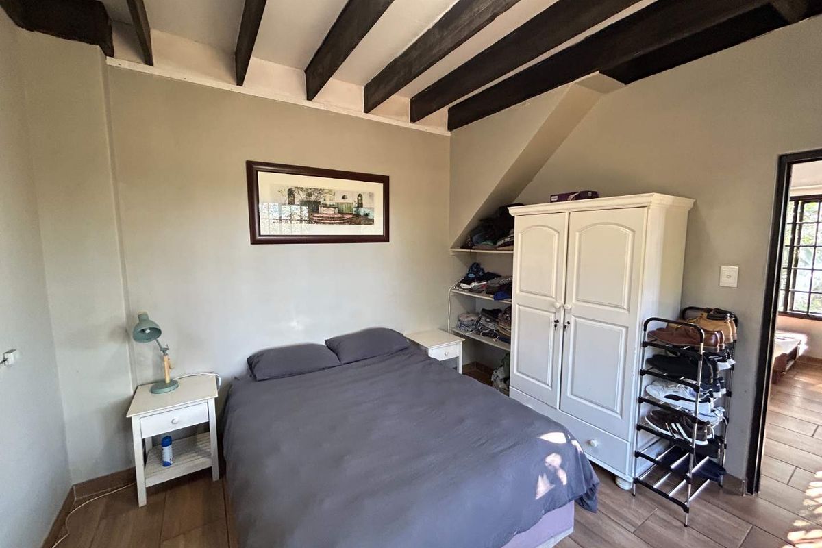 A cozy bedroom featuring exposed timber ceiling beams and tiled flooring, offering a rustic cottage aesthetic.