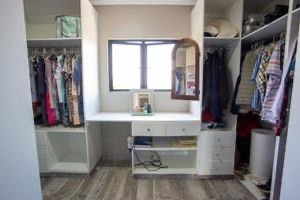 A walk-in closet featuring built-in white cabinetry, hanging rails, shelving, and a central vanity desk area with a window.