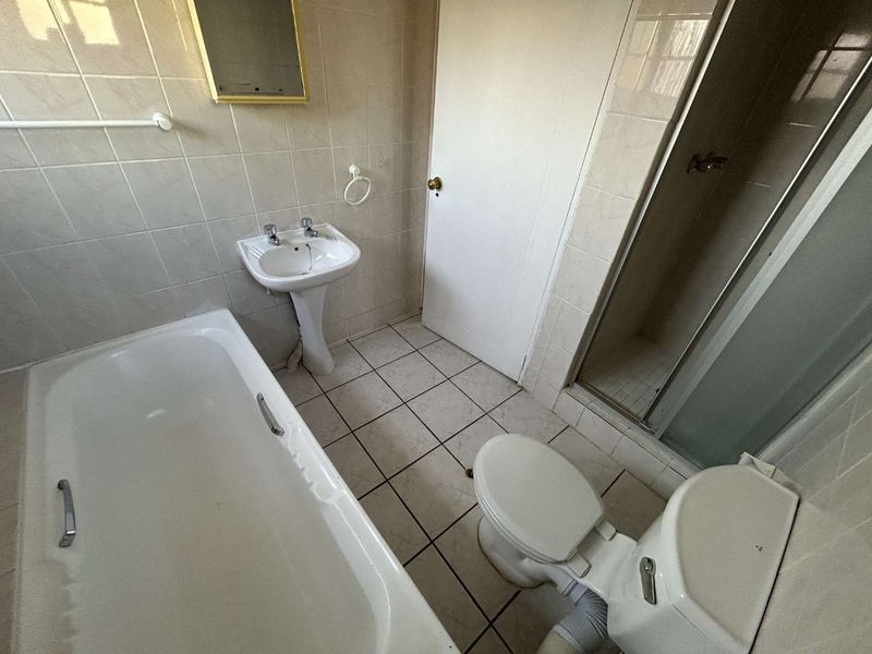 A functional bathroom featuring a pedestal basin, bathtub, separate shower enclosure, and toilet with neutral wall and floor tiling.