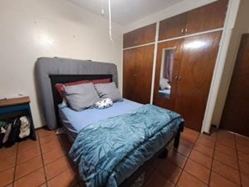 A bedroom featuring built-in wooden cupboards with a mirrored panel and tiled flooring, offering functional storage space in need of cosmetic updates.