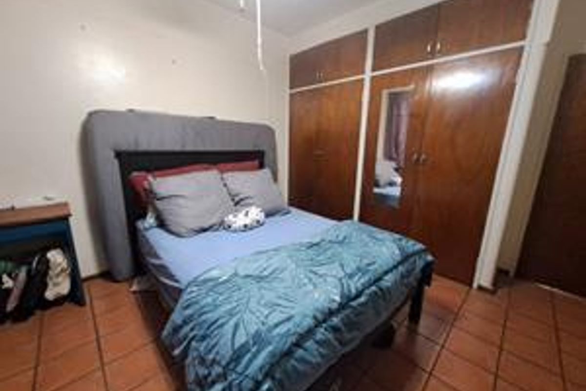 A bedroom featuring built-in wooden cupboards with a mirrored panel and tiled flooring, offering functional storage space in need of cosmetic updates.