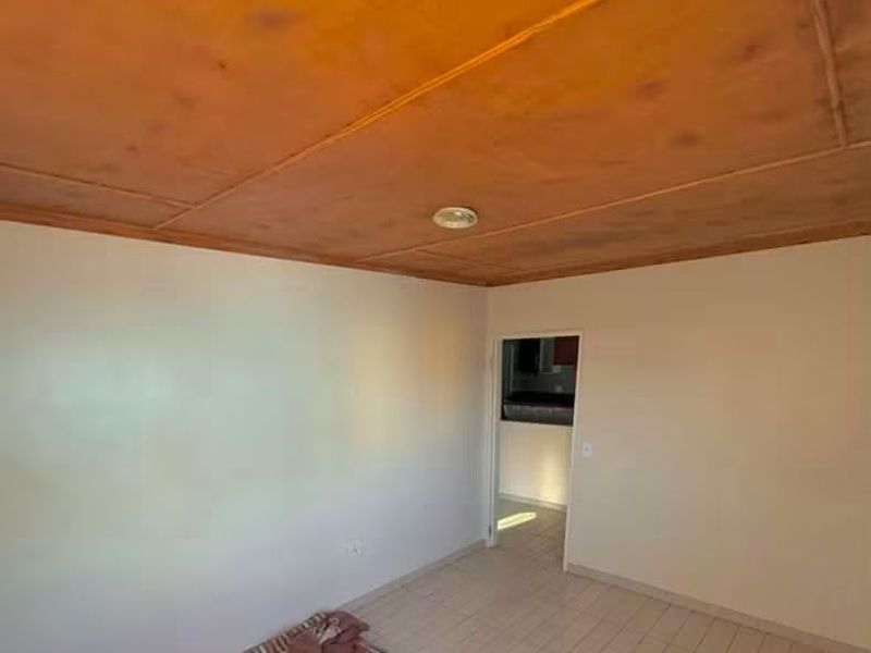 A simple living area featuring tiled flooring and a wooden panel ceiling, offering a blank canvas for potential interior updates.