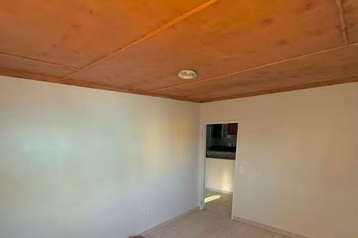 A simple living area featuring tiled flooring and a wooden panel ceiling, offering a blank canvas for potential interior updates.