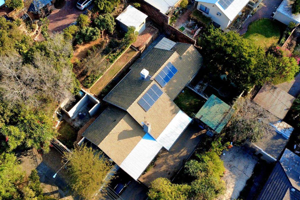 Aerial view of the property showing the roof structure, installed solar panels, surrounding garden, and paved driveway area.