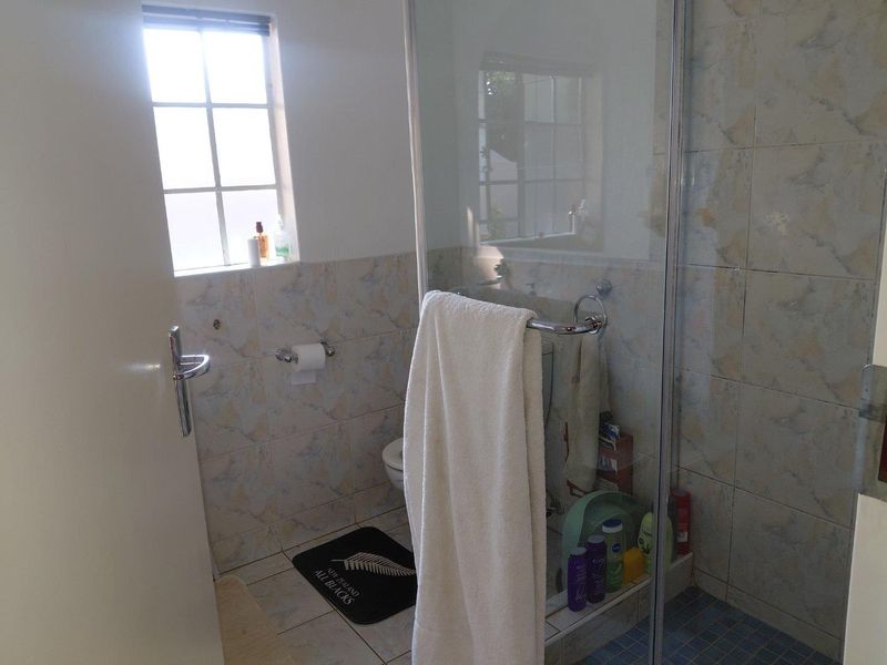 A functional bathroom featuring a glass-enclosed shower, toilet, and neutral wall tiling, providing a practical space with natural light from the window.