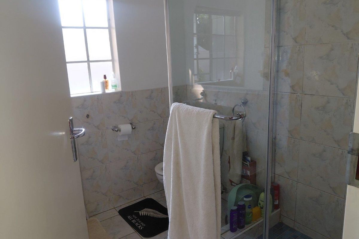 A functional bathroom featuring a glass-enclosed shower, toilet, and neutral wall tiling, providing a practical space with natural light from the window.