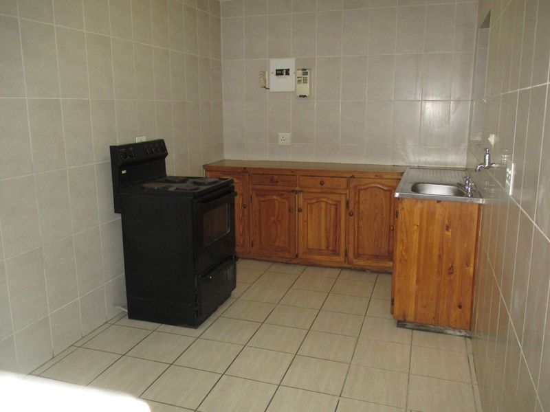 A functional kitchen featuring tiled walls and floors, wooden cabinetry, a stainless steel sink, and a freestanding stove.