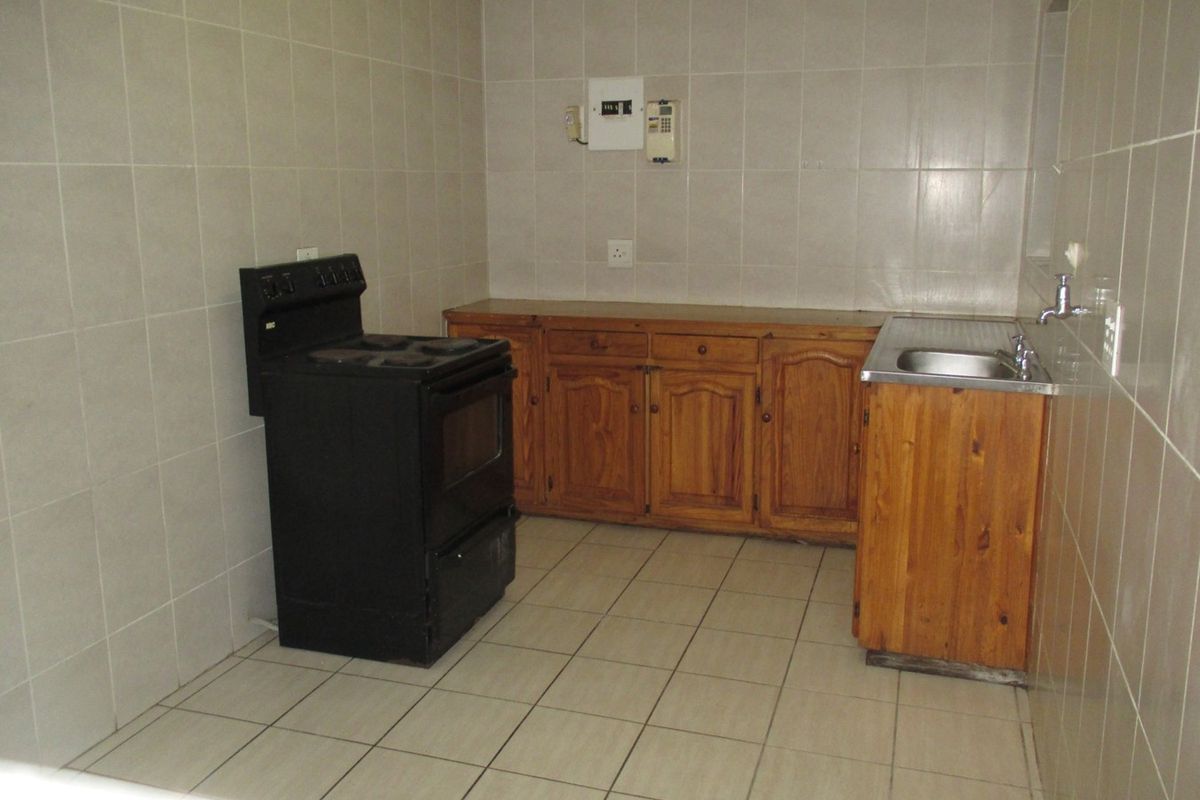 A functional kitchen featuring tiled walls and floors, wooden cabinetry, a stainless steel sink, and a freestanding stove.