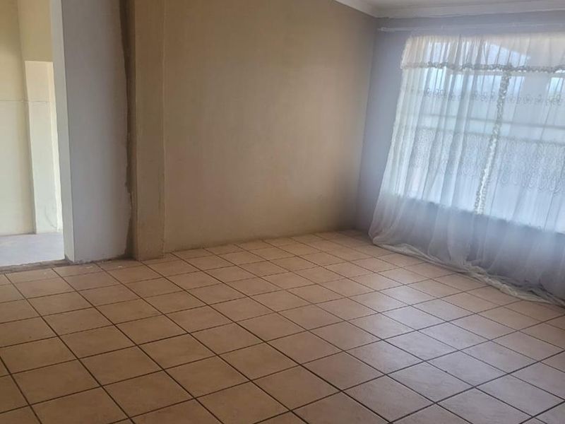 An empty living room featuring tiled flooring and an exposed timber beam, currently requiring final wall finishing and painting.