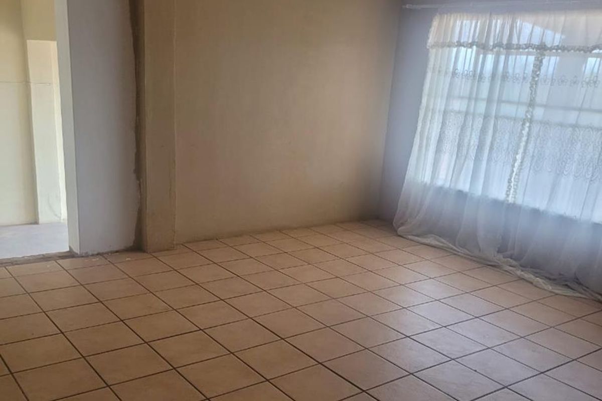 An empty living room featuring tiled flooring and an exposed timber beam, currently requiring final wall finishing and painting.