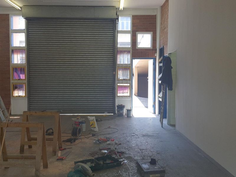 Industrial garage space featuring exposed brick walls, concrete flooring, and a large roller shutter door, currently undergoing maintenance or renovation.