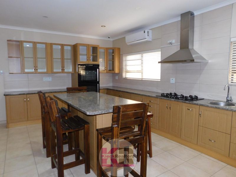 Modern kitchen featuring light wood cabinetry, granite countertops, a central island, built-in oven, gas hob, and an integrated extractor fan.