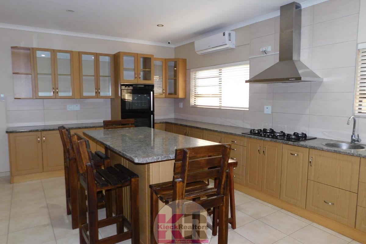 Modern kitchen featuring light wood cabinetry, granite countertops, a central island, built-in oven, gas hob, and an integrated extractor fan.