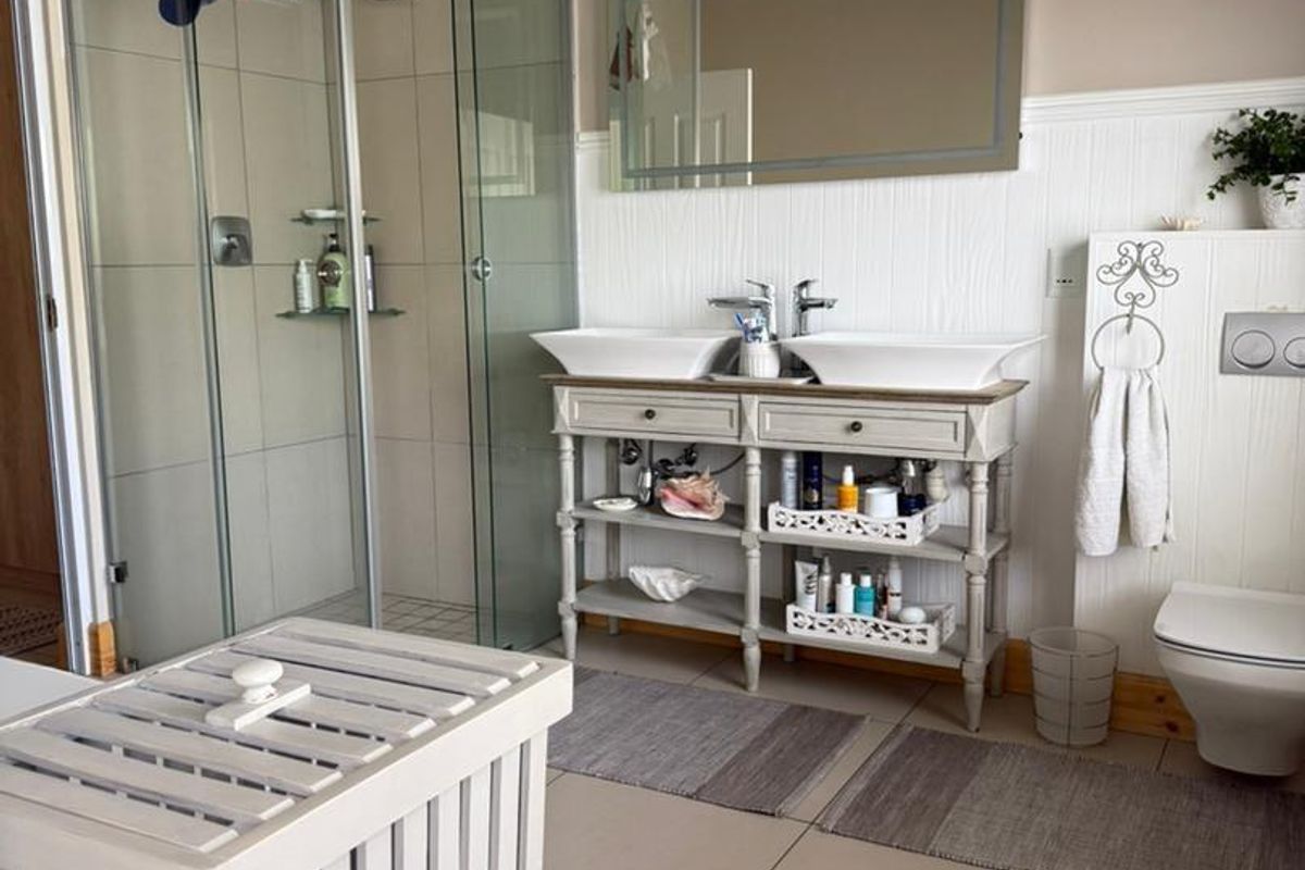 A bathroom featuring a glass-enclosed shower, a double vanity with vessel sinks, and a wall-mounted toilet with a concealed cistern.