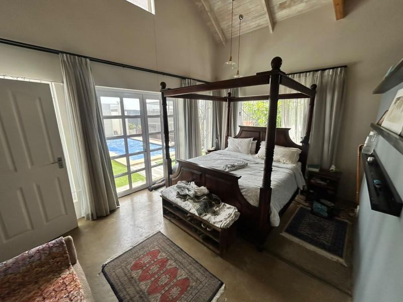 Spacious bedroom featuring a high vaulted ceiling with exposed timber beams, polished concrete floors, and direct access to the pool area via french doors.